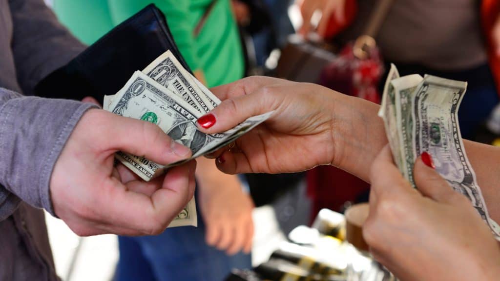 One person's hands giving several dollar bills to another person's hand